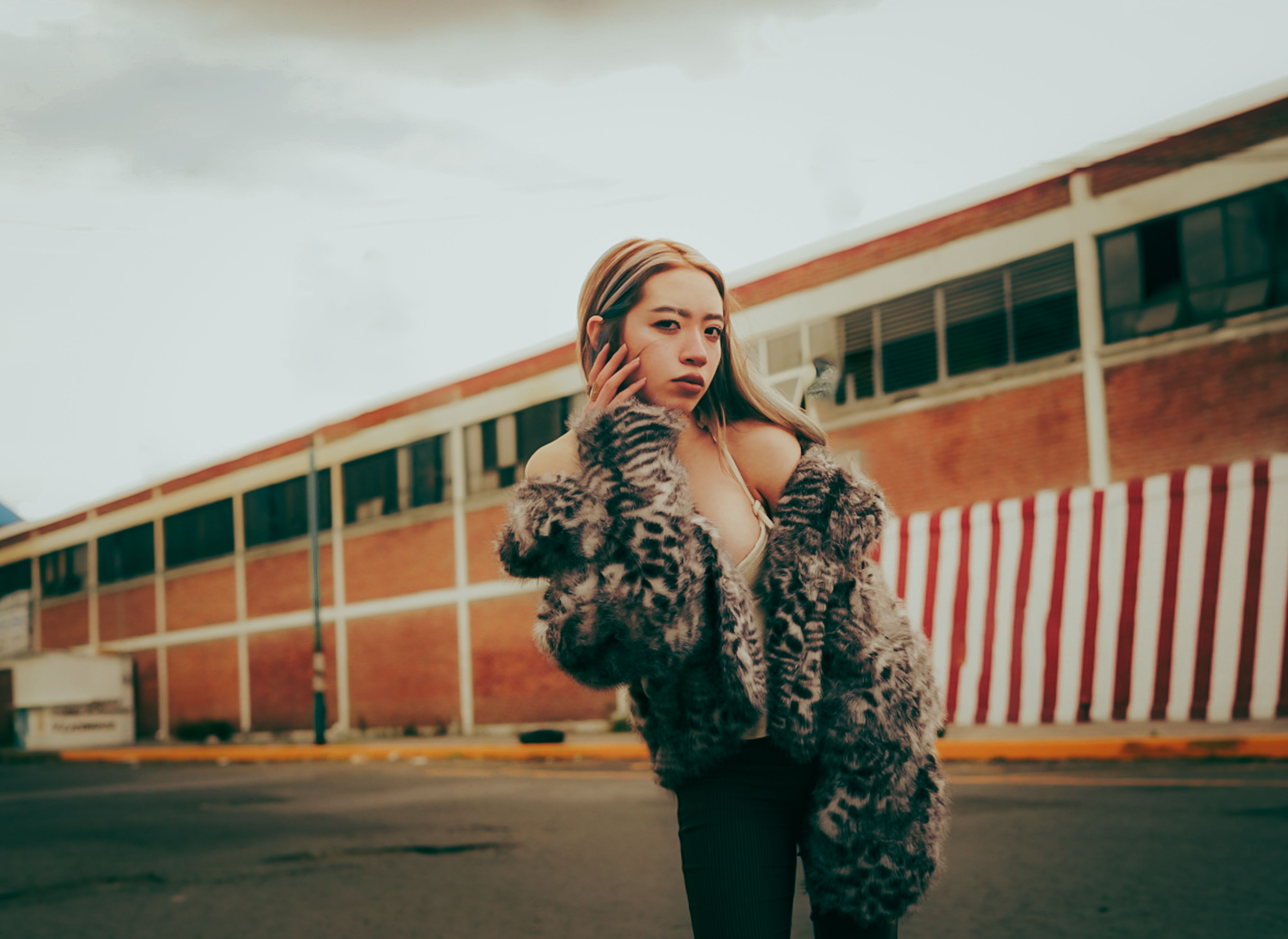 Fashionable woman in a fur coat posing stylishly against an industrial urban backdrop.