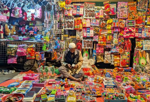 A street vendor sits among a vibrant display of colorful toys at a night market.