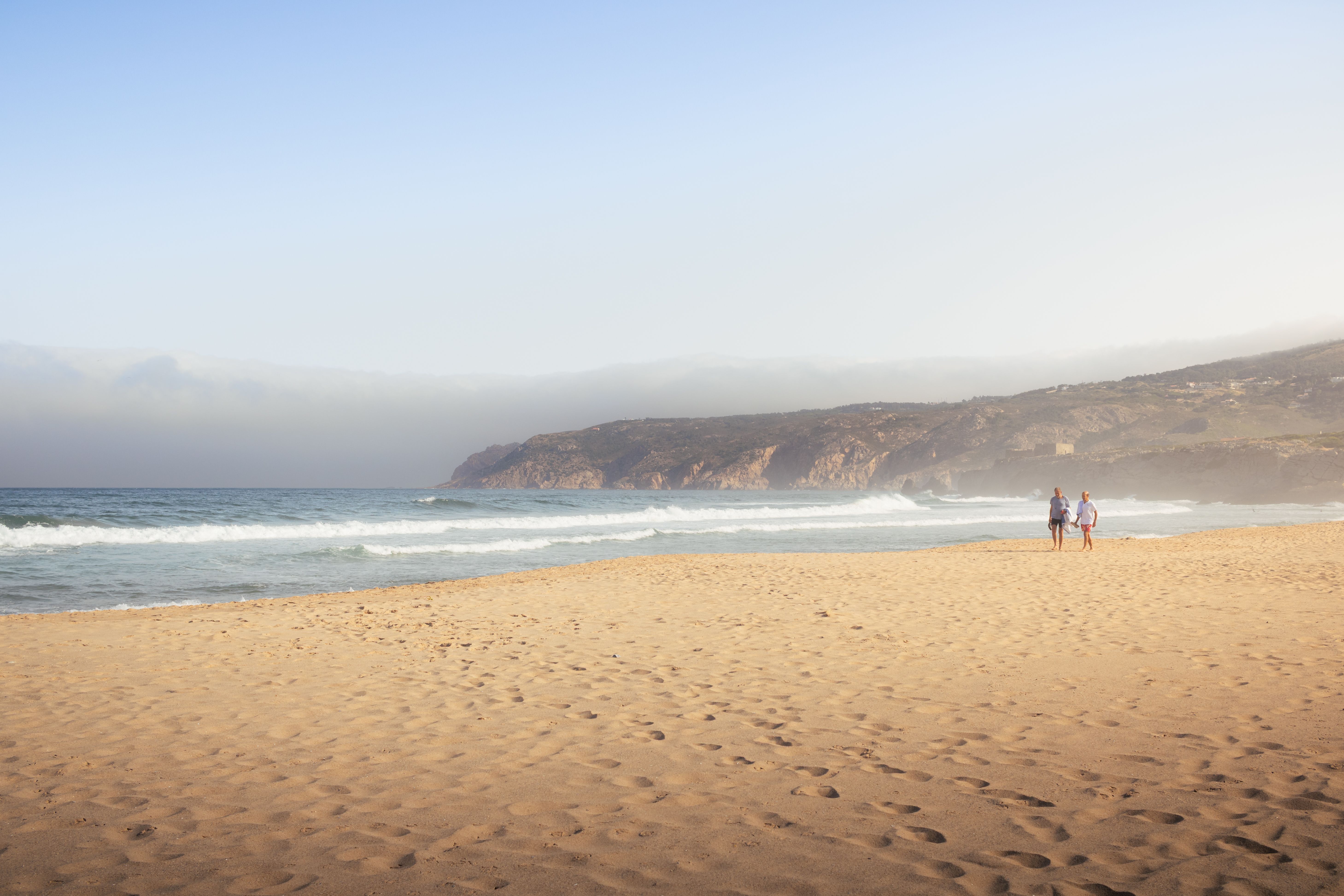 A tranquil beach scene in Cascais, Portugal, with waves and hills under a clear sky.