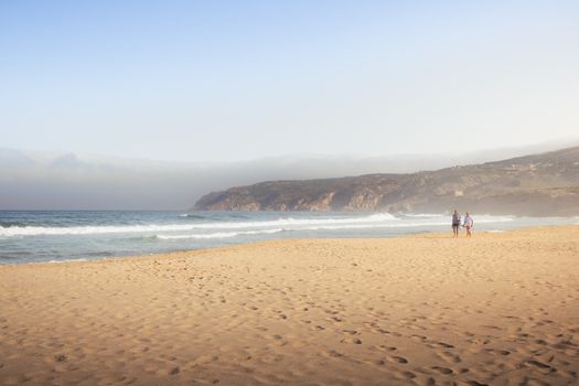 A tranquil beach scene in Cascais, Portugal, with waves and hills under a clear sky.