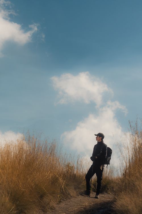 Free A lone hiker stands on a grassy path, gazing at clouds under a clear blue sky in Puebla, México. Stock Photo