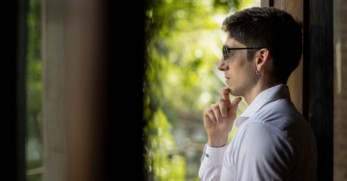 Jovem em camisa branca observa pensativamente pela janela em Buenos Aires.