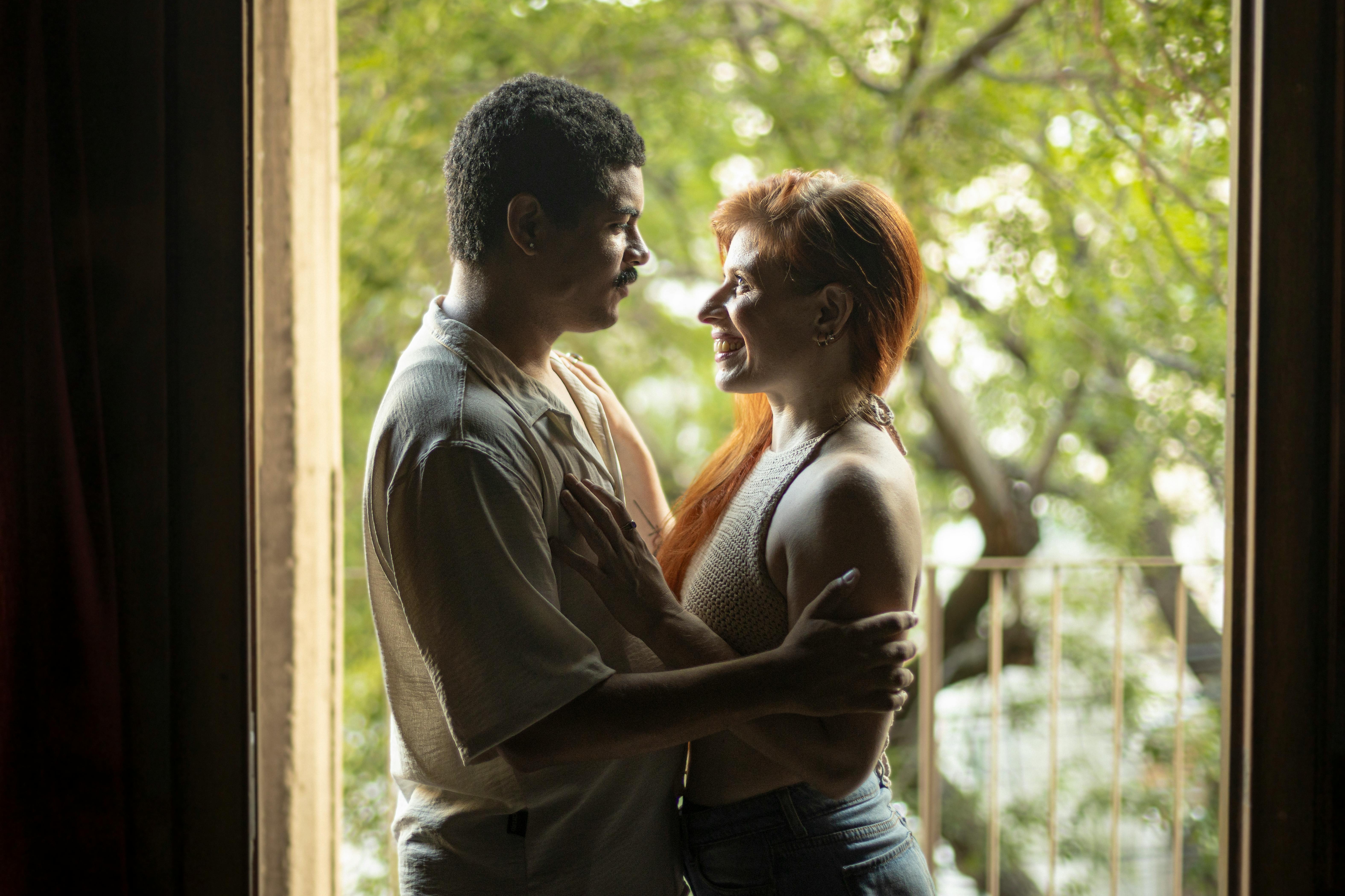 Intimate couple embracing closely in dim light, bodies pressed in trusting closeness