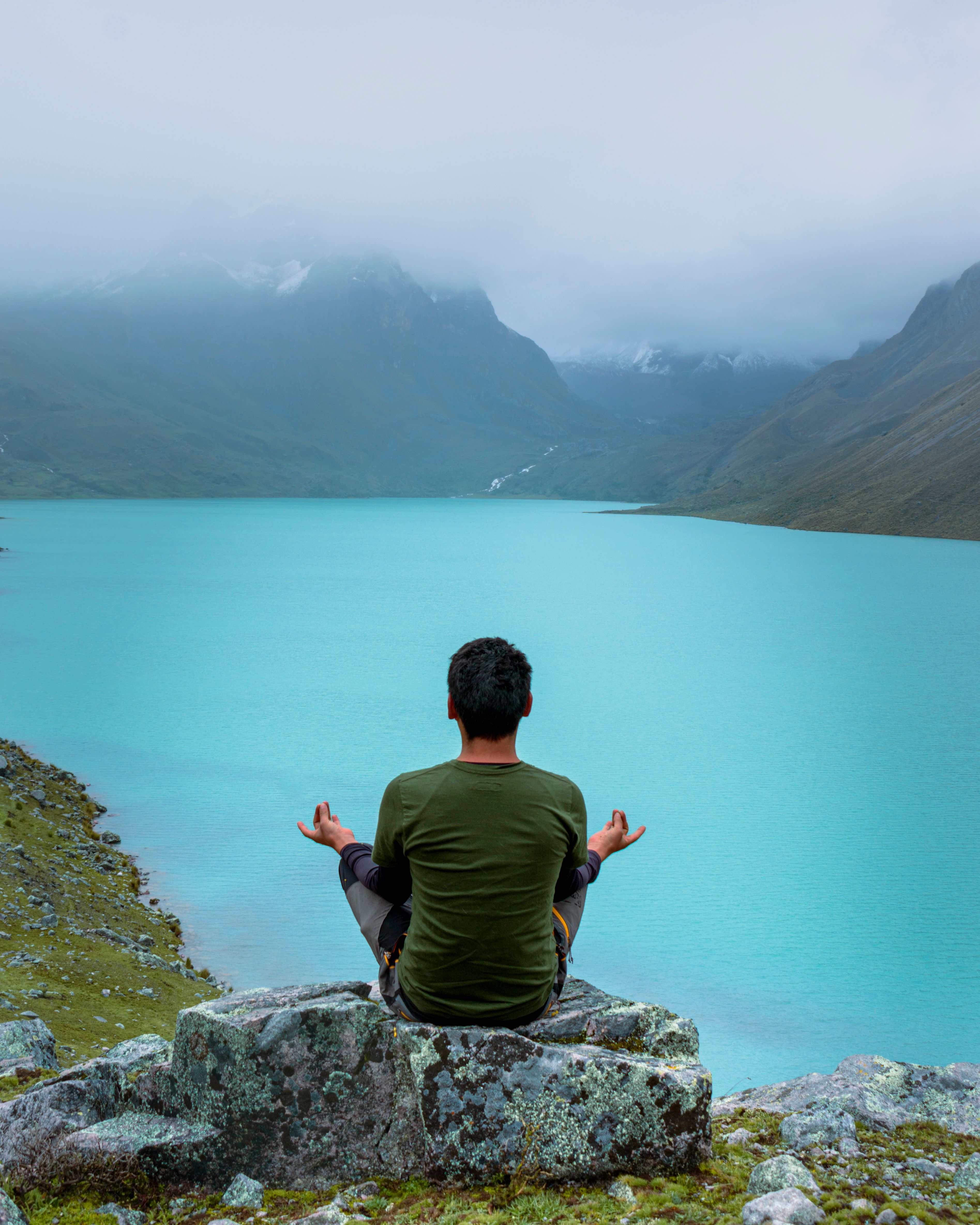Man sitting on rocks overlooking a serene turquoise lake in the Andes mountains, Cusco, Peru.