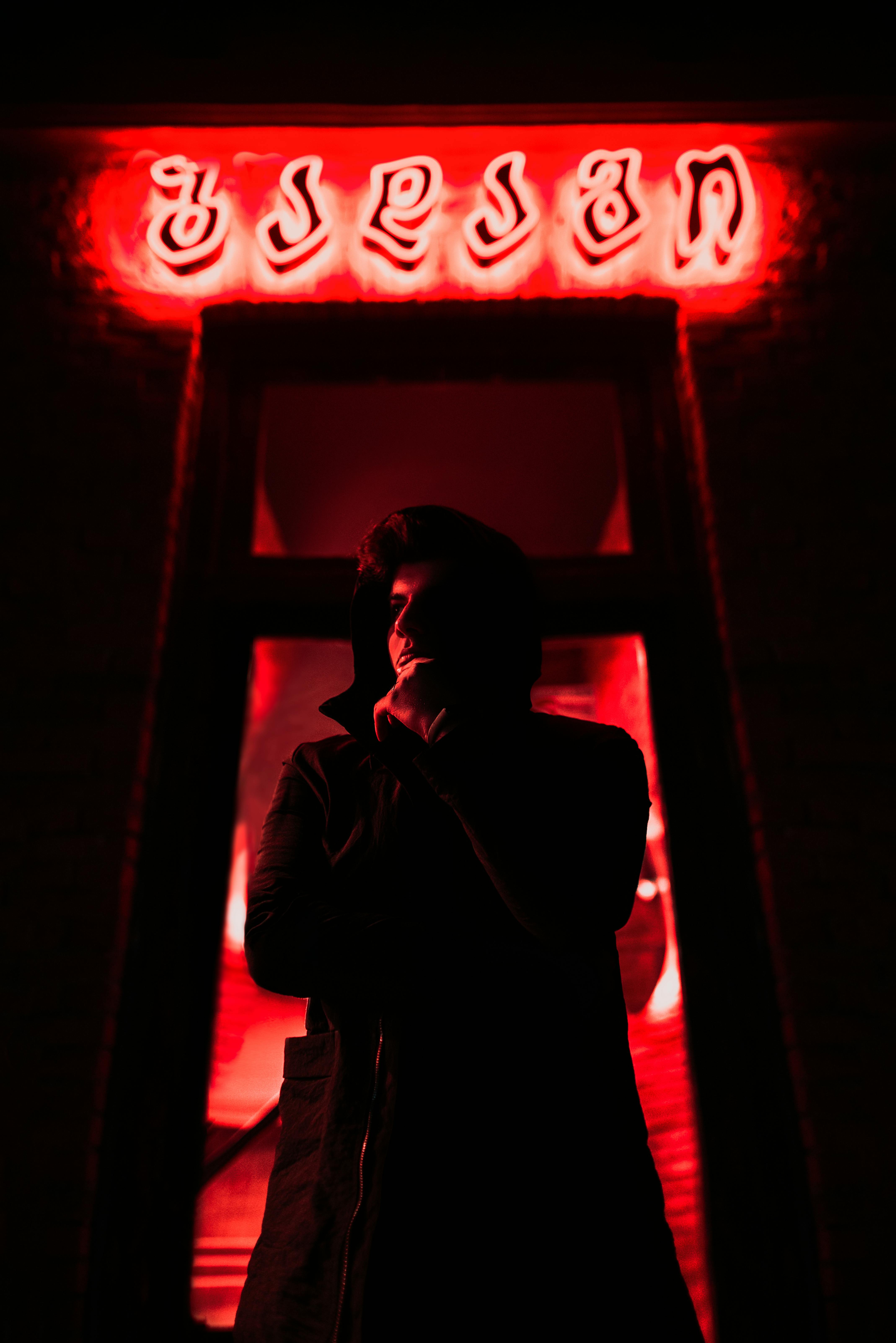A mysterious silhouette of a man stands under a red neon-lit entrance in Kutaisi, Georgia, creating a moody and dramatic scene.