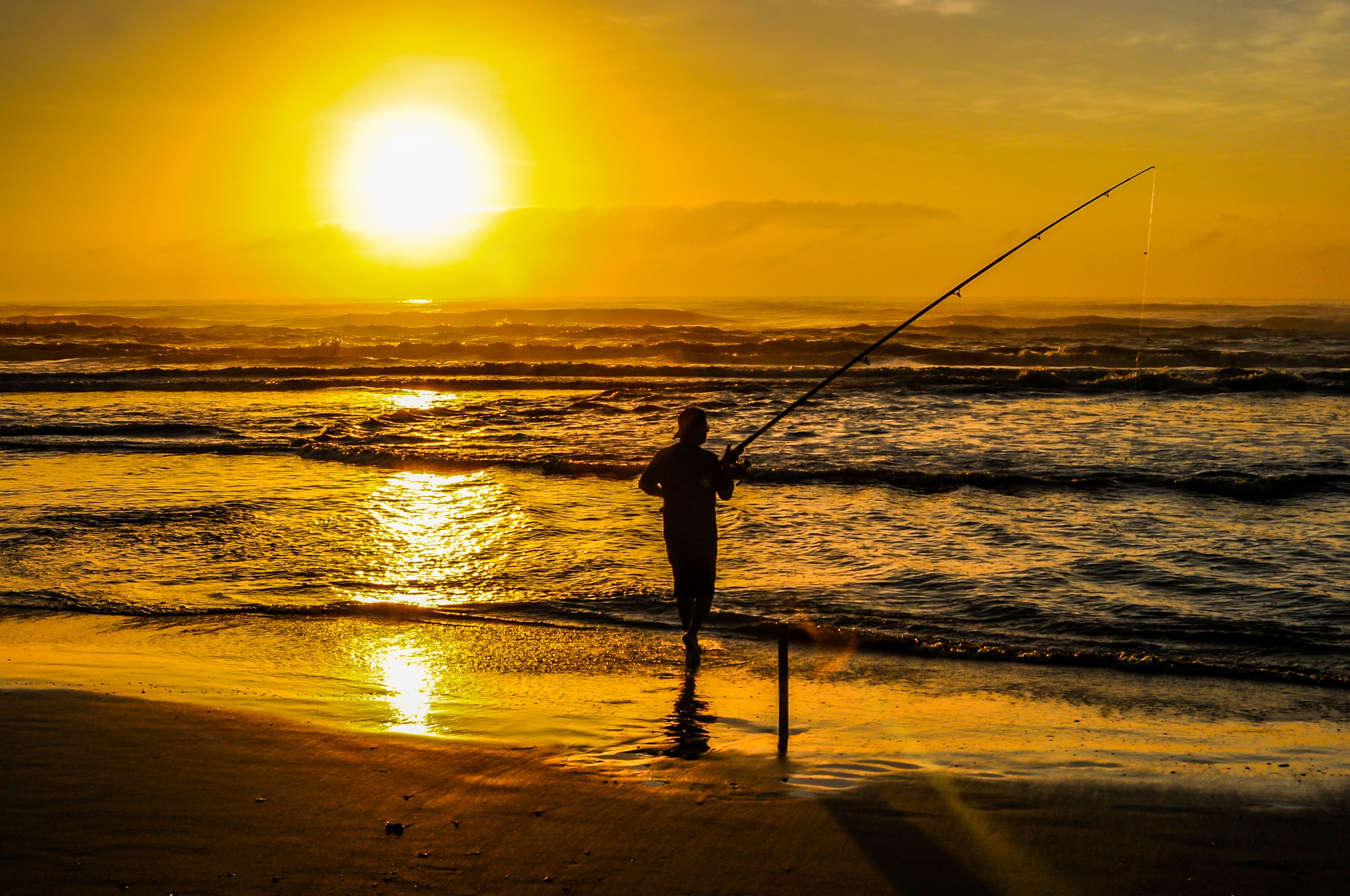Silhouette of a fisherman casting a line into the ocean at sunrise, with golden sunlight reflecting on the water.