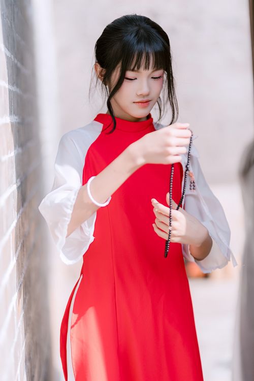 Free Teen girl in a red dress holding beads, standing in an alleyway, captured with soft lighting. Stock Photo