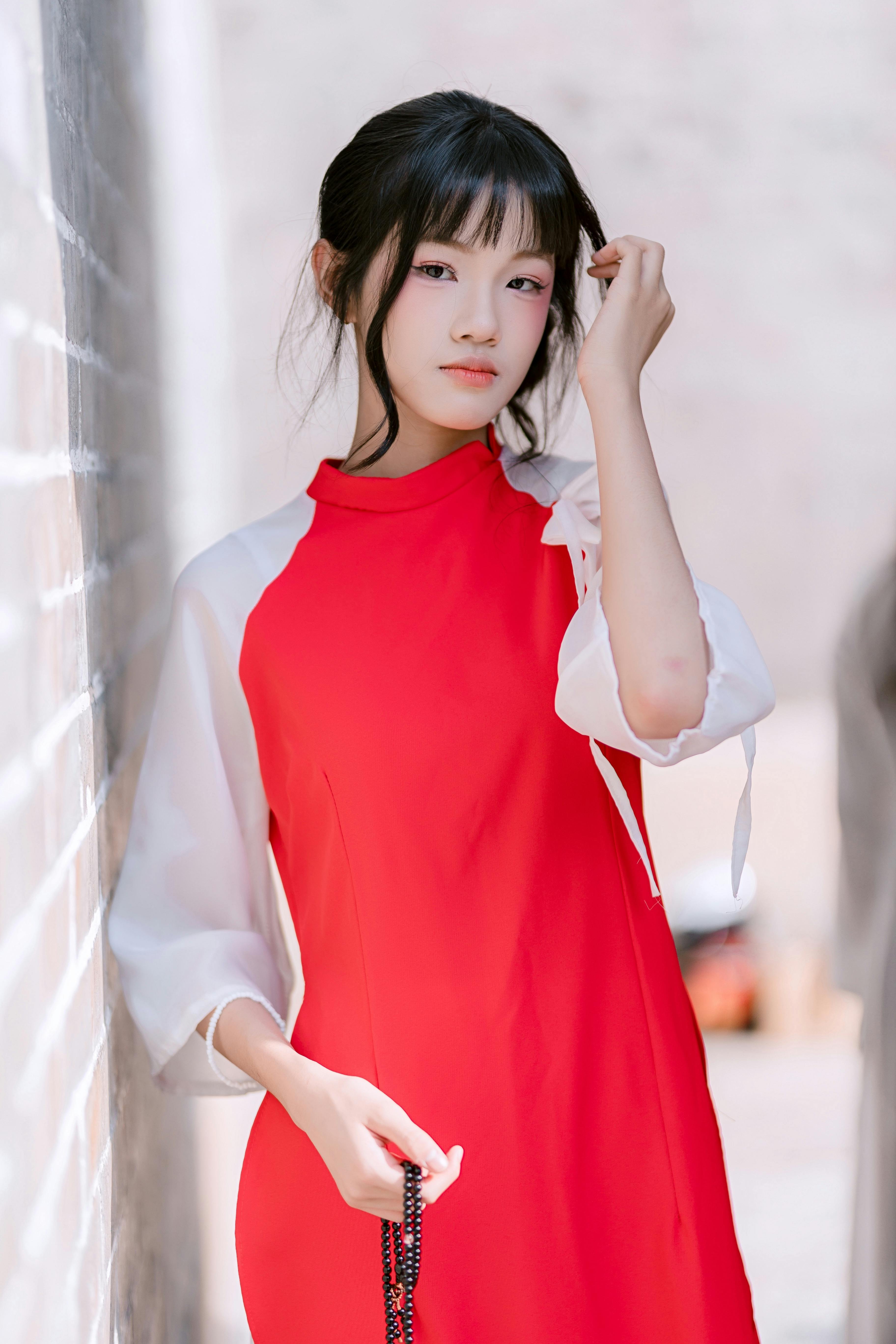 Stylish woman in a vibrant red dress poses confidently outdoors during the day.