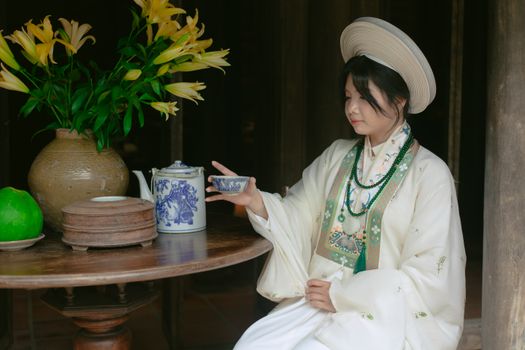 A woman in traditional attire enjoying tea amid elegant floral arrangements.