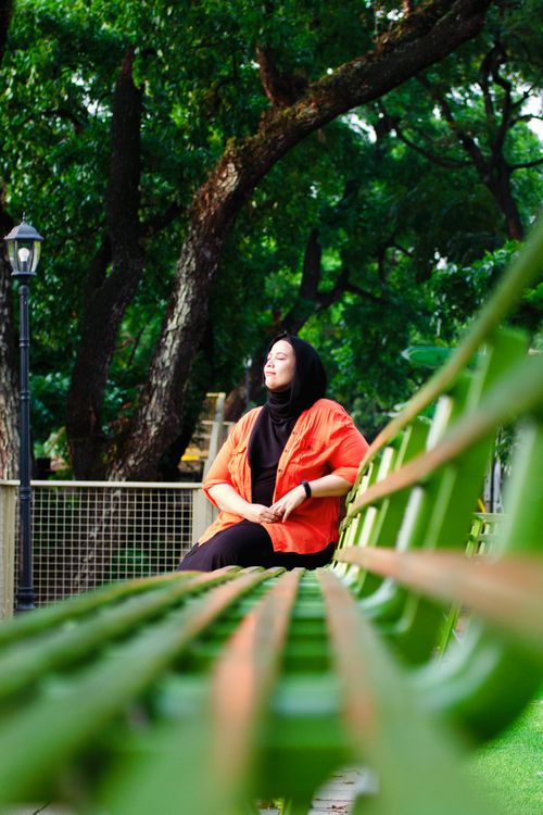 Free Woman in a park enjoying a serene moment on a bench surrounded by lush greenery. Stock Photo