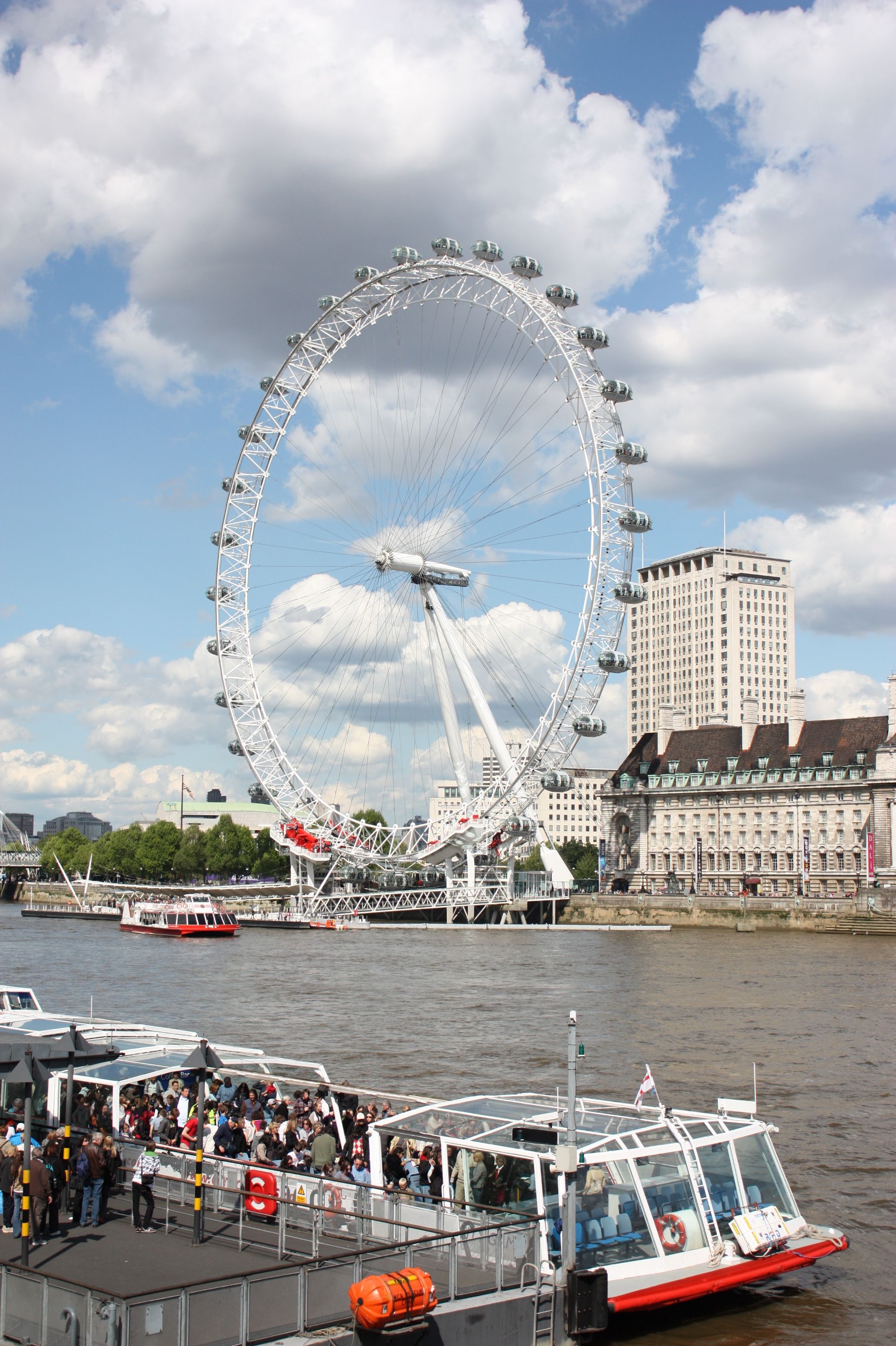 The London Eye Pier on the Thames South Bank with the London Eye wheel rising overhead and passengers boarding a river cruise boat
