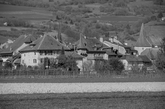 Black and white photo of traditional Swiss village architecture with fields and hills in the background.
