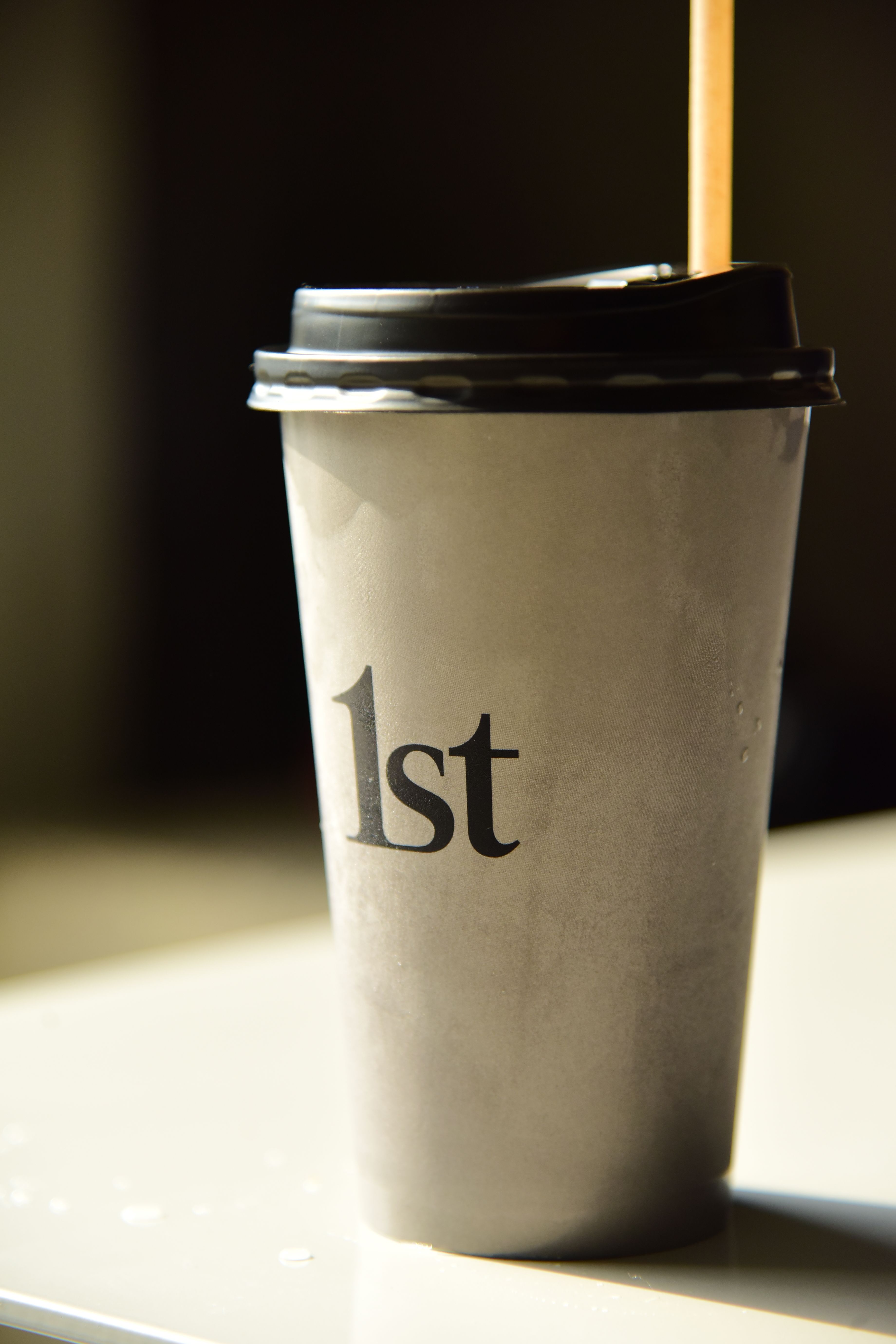 A gray coffee cup labeled '1st' with a black lid and straw, perfect for branding.