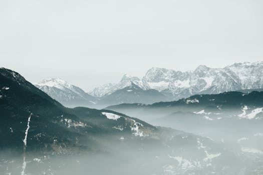 Serene view of a misty, snow-covered alpine mountain range, perfect for winter landscapes.