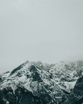 A dramatic snow-covered mountain range under overcast skies in the Alps, Europe.