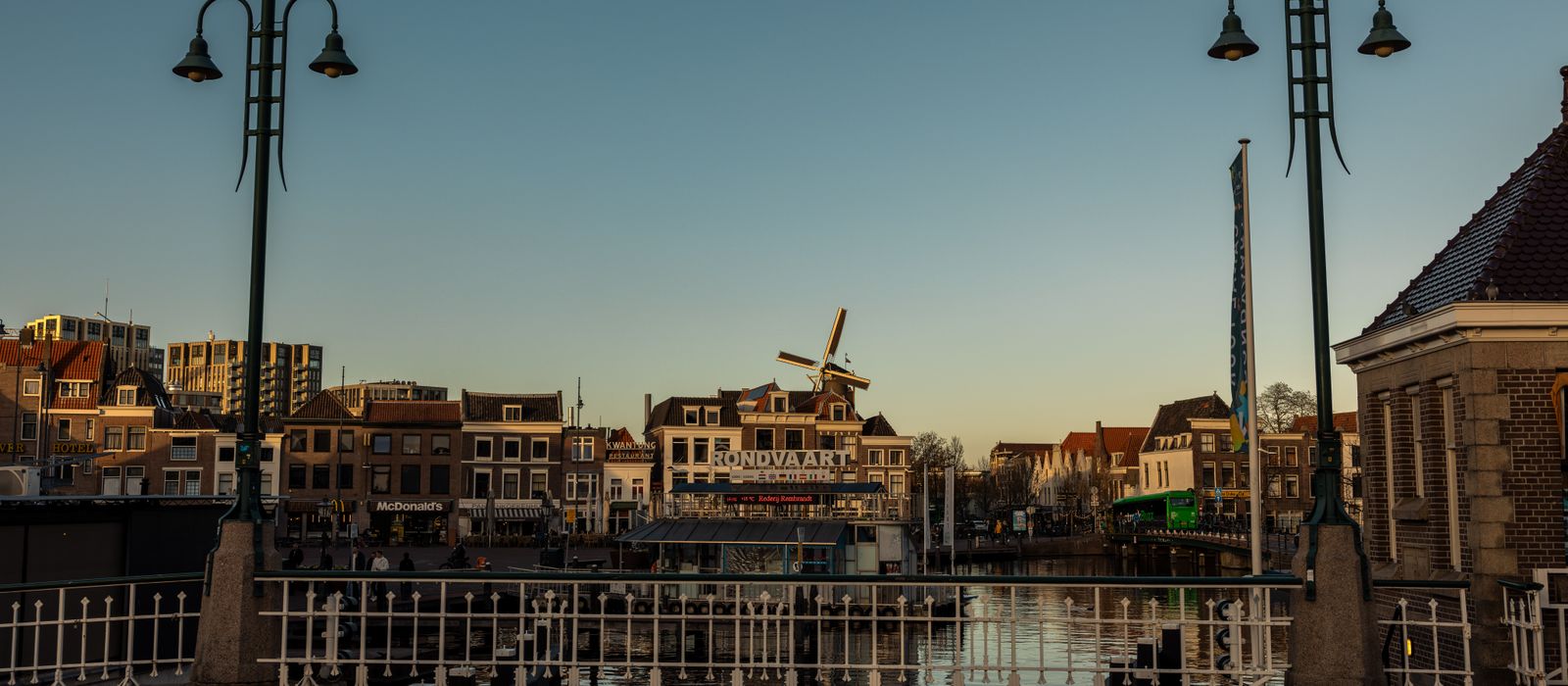 Picturesque Leiden cityscape with canal, bridge, and windmill at twilight. Historic Dutch architecture under a clear sky.