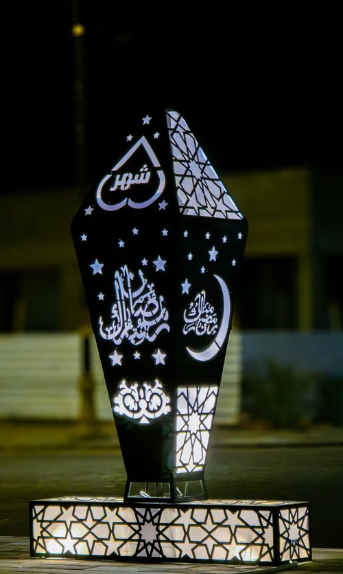 Free Elegant outdoor lantern with Arabic script illuminated against a dark night backdrop, featuring stars and crescent moon. Stock Photo