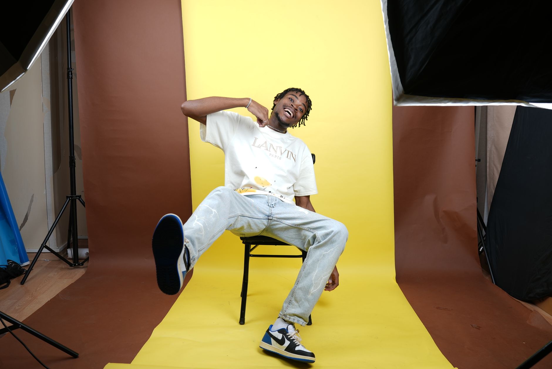 A trendy young man poses playfully in a professional studio setting with a colorful backdrop.