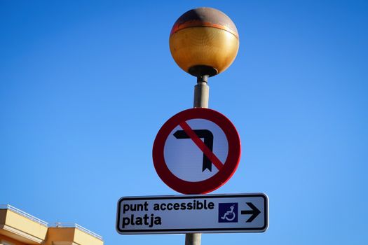 No left turn sign with accessible beach direction in Cala Millor, Spain.