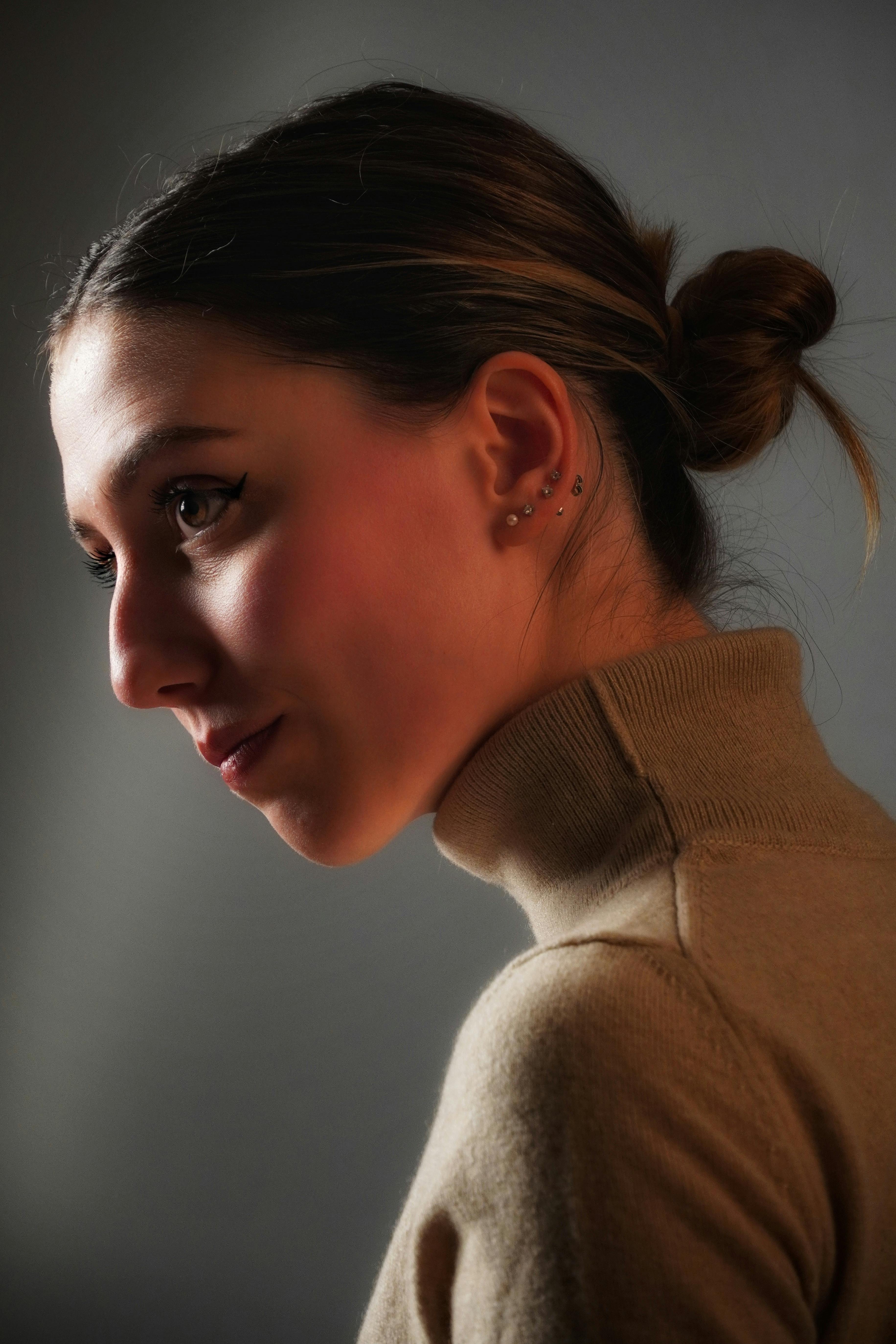 Δωρεάν Κοντινό πλάνο προφίλ μιας γυναίκας με χτένισμα σε κότσο, που φοράει σκουλαρίκια με καρφωτά, σε απαλό ζεστό φως. Φωτογραφία από στοκ φωτογραφιών