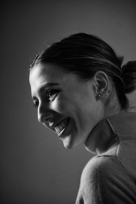Black and white portrait of a young woman smiling, exuding elegance and warmth in soft lighting.