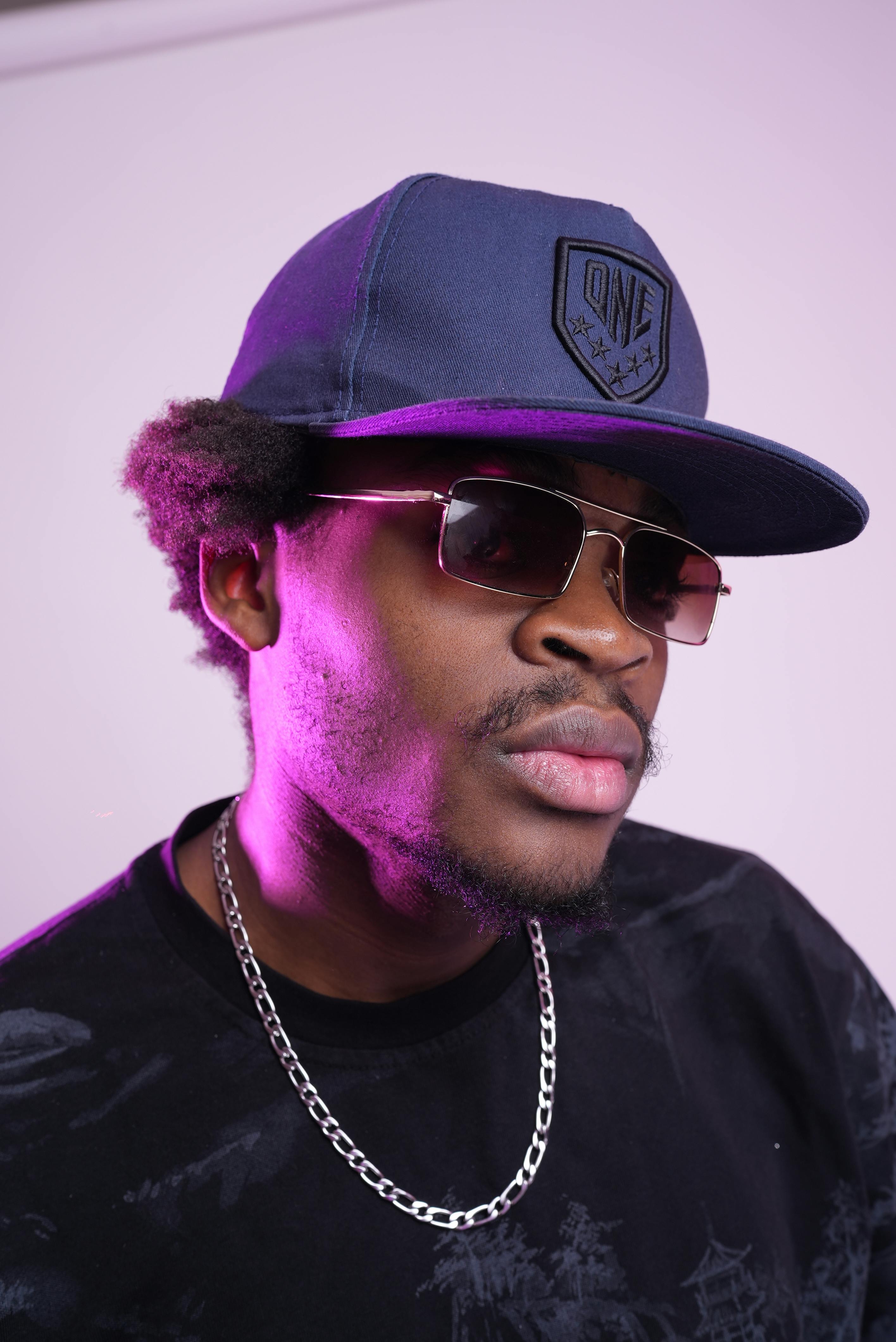 Portrait of a fashionable man wearing sunglasses and a cap with purple lighting.