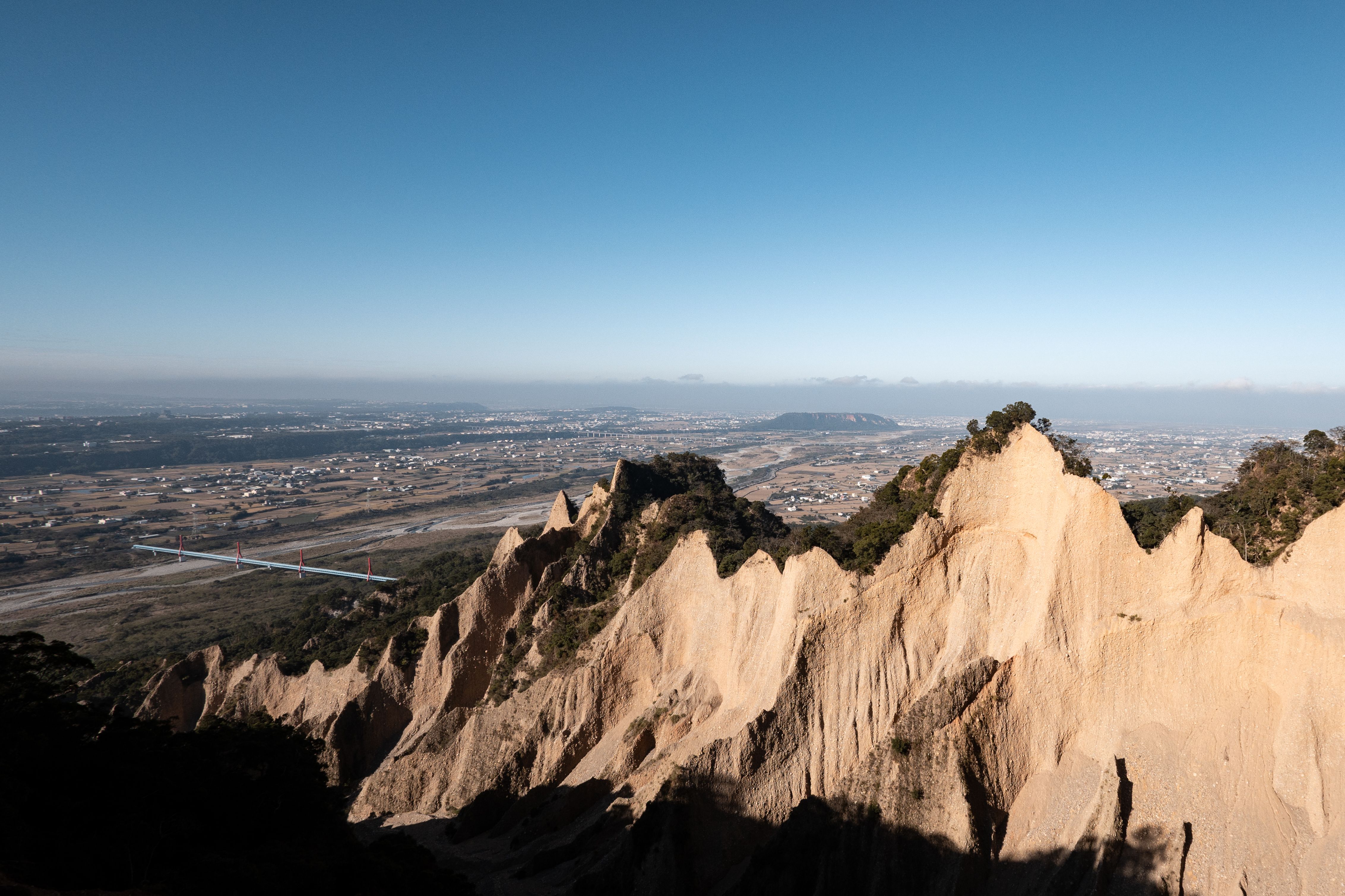 Panoramic landscape of extraordinary rock formations at Badlands, Miaoli County, Taiwan under a clear blue sky.