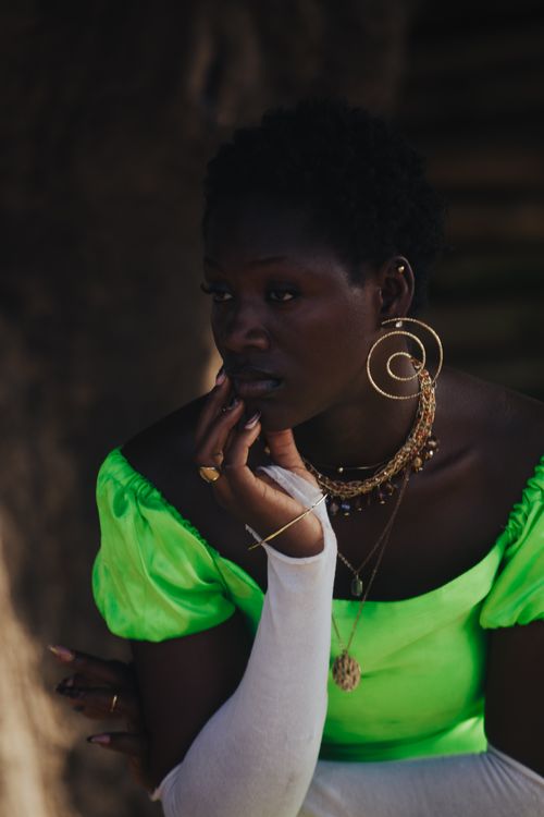 Free A thoughtful woman in vibrant attire with bold accessories, captured beautifully in soft lighting. Stock Photo