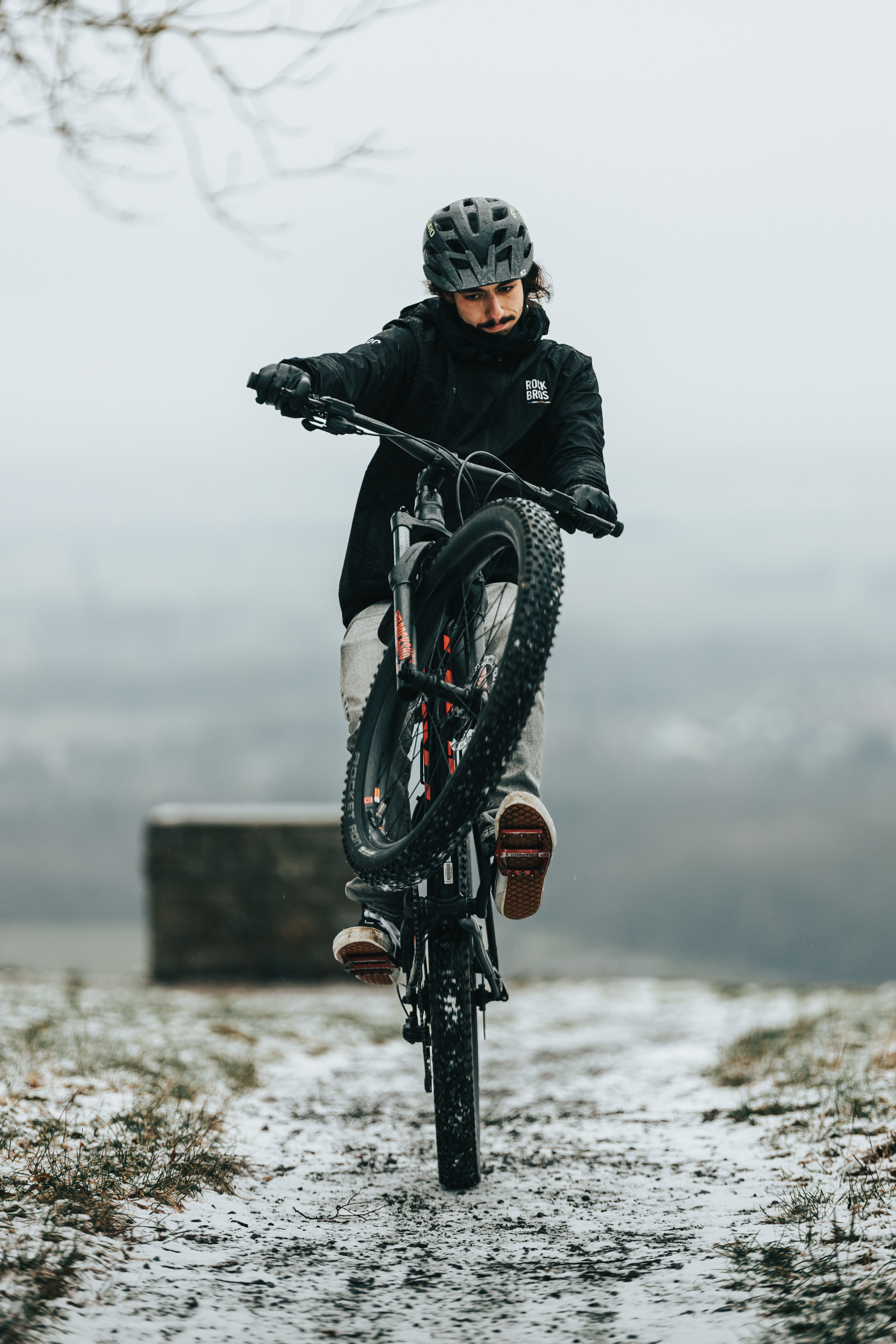Mountain biker executing a wheelie on a snowy path, showcasing skill and balance in winter conditions.