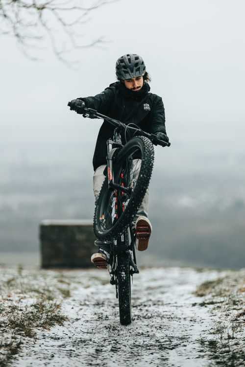 Free Mountain biker executing a wheelie on a snowy path, showcasing skill and balance in winter conditions. Stock Photo