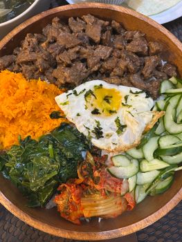 Vibrant Korean bibimbap with beef, vegetables, and fried egg in a rustic wooden bowl.