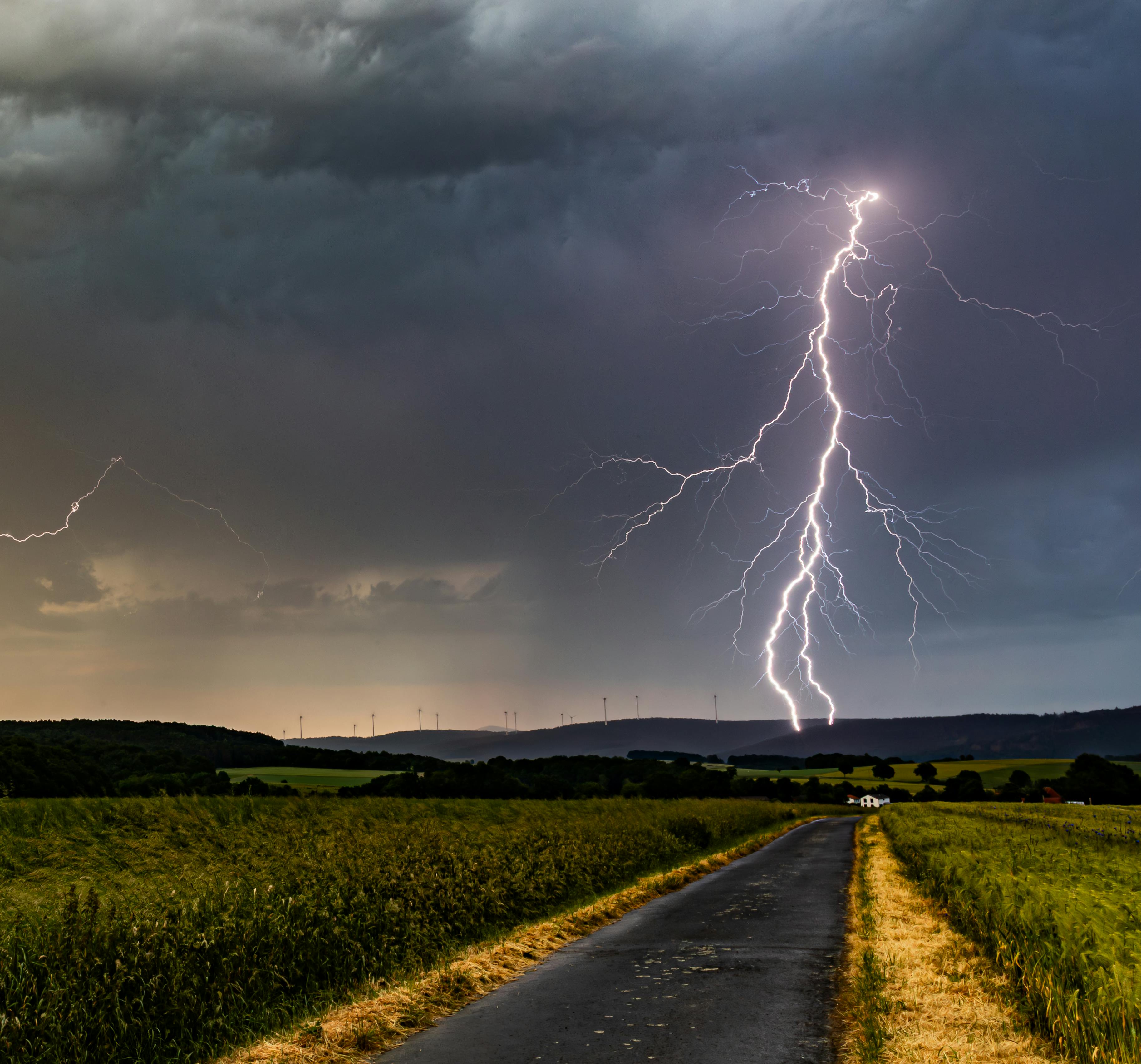 Striking landscape with a lightning bolt hitting near a rural road under a stormy sky.
