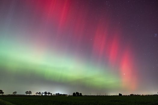 Vibrant red and green aurora borealis in a starry night sky over a tranquil landscape.