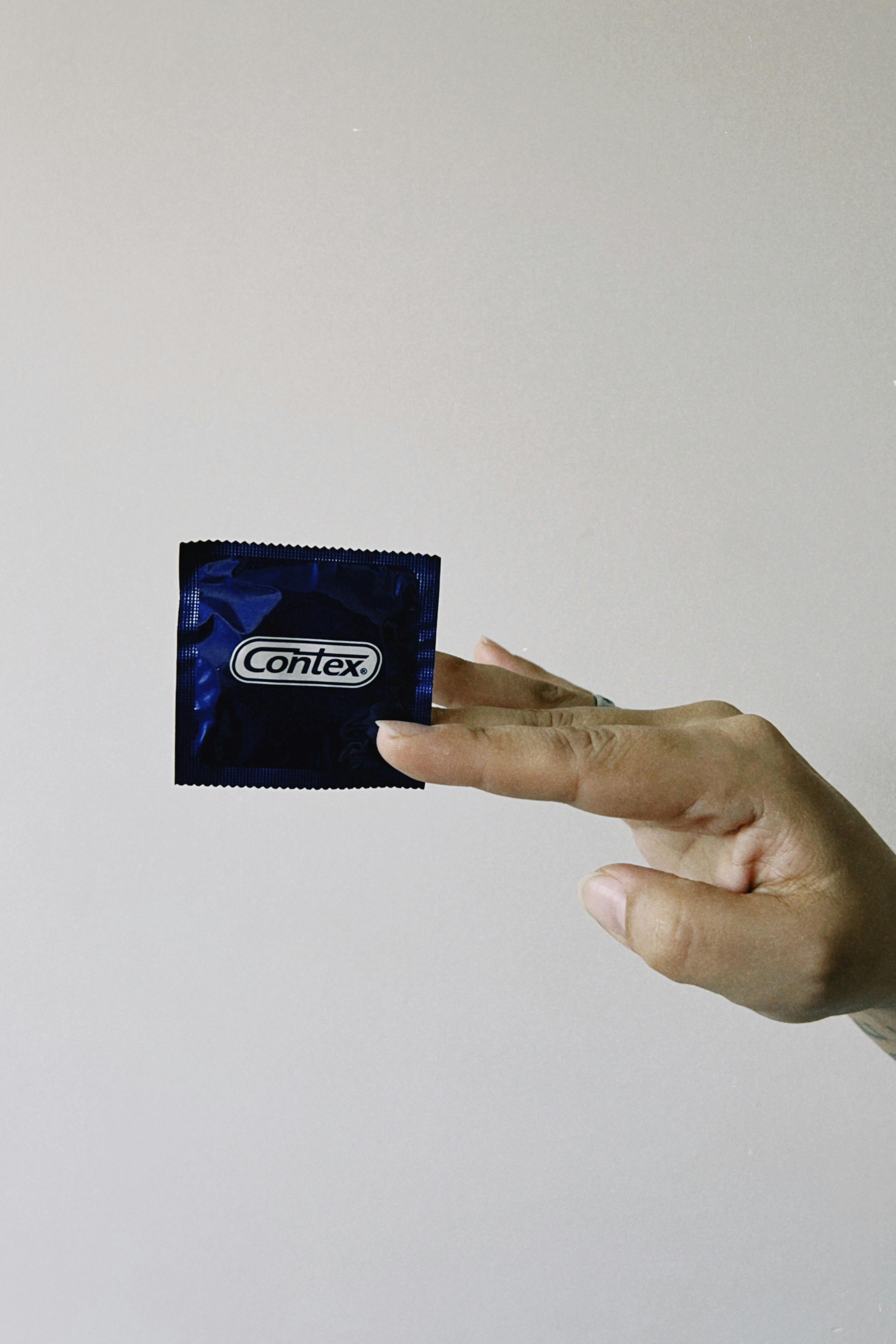 grátis Mão segurando um pacote de preservativo azul, promovendo sexo seguro em um fundo neutro. Foto profissional