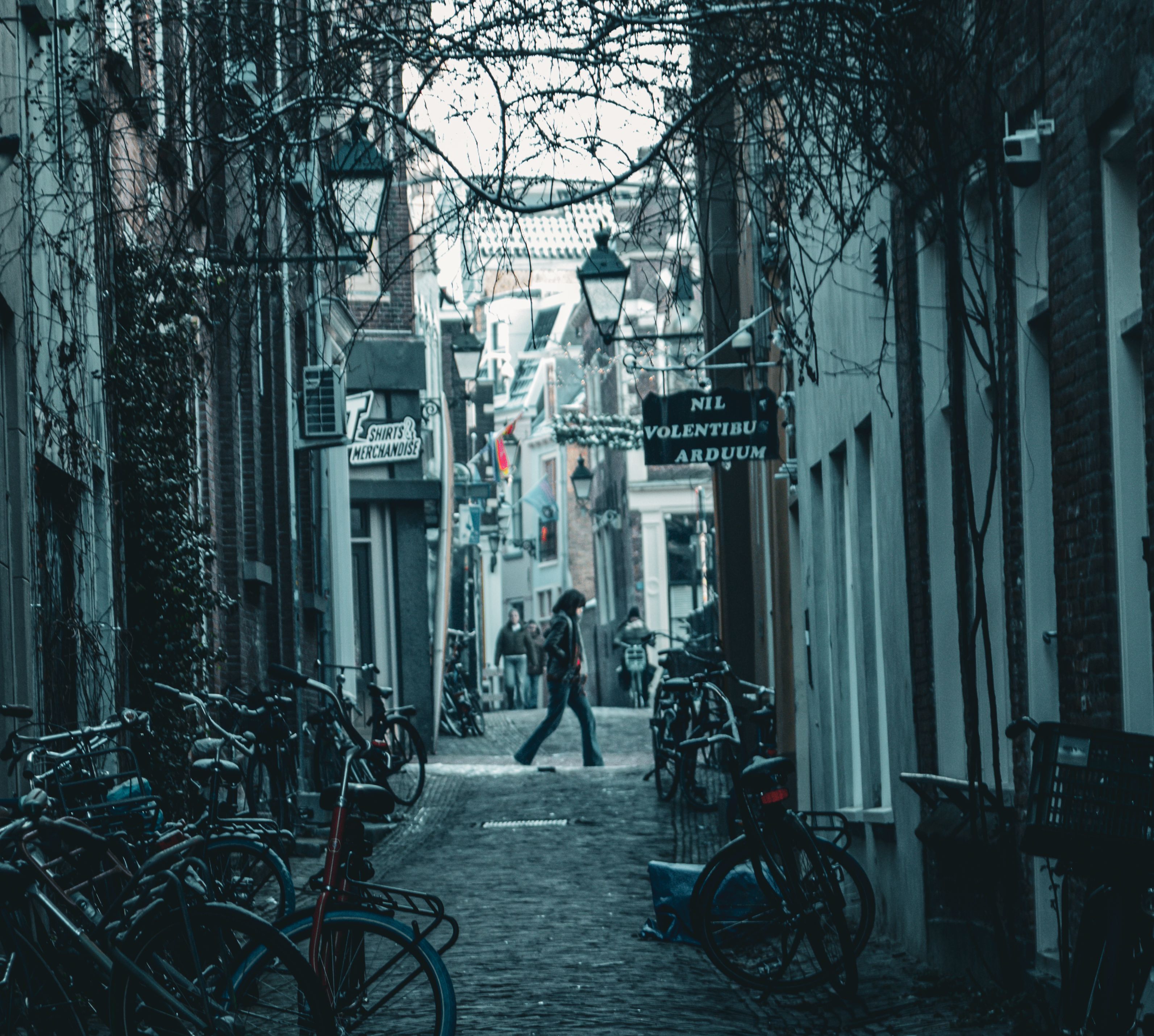 A narrow European alley with bicycles lined up and people walking through, capturing urban charm.