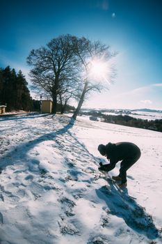 Man photographing snow-covered landscape with a lone tree under bright sun.