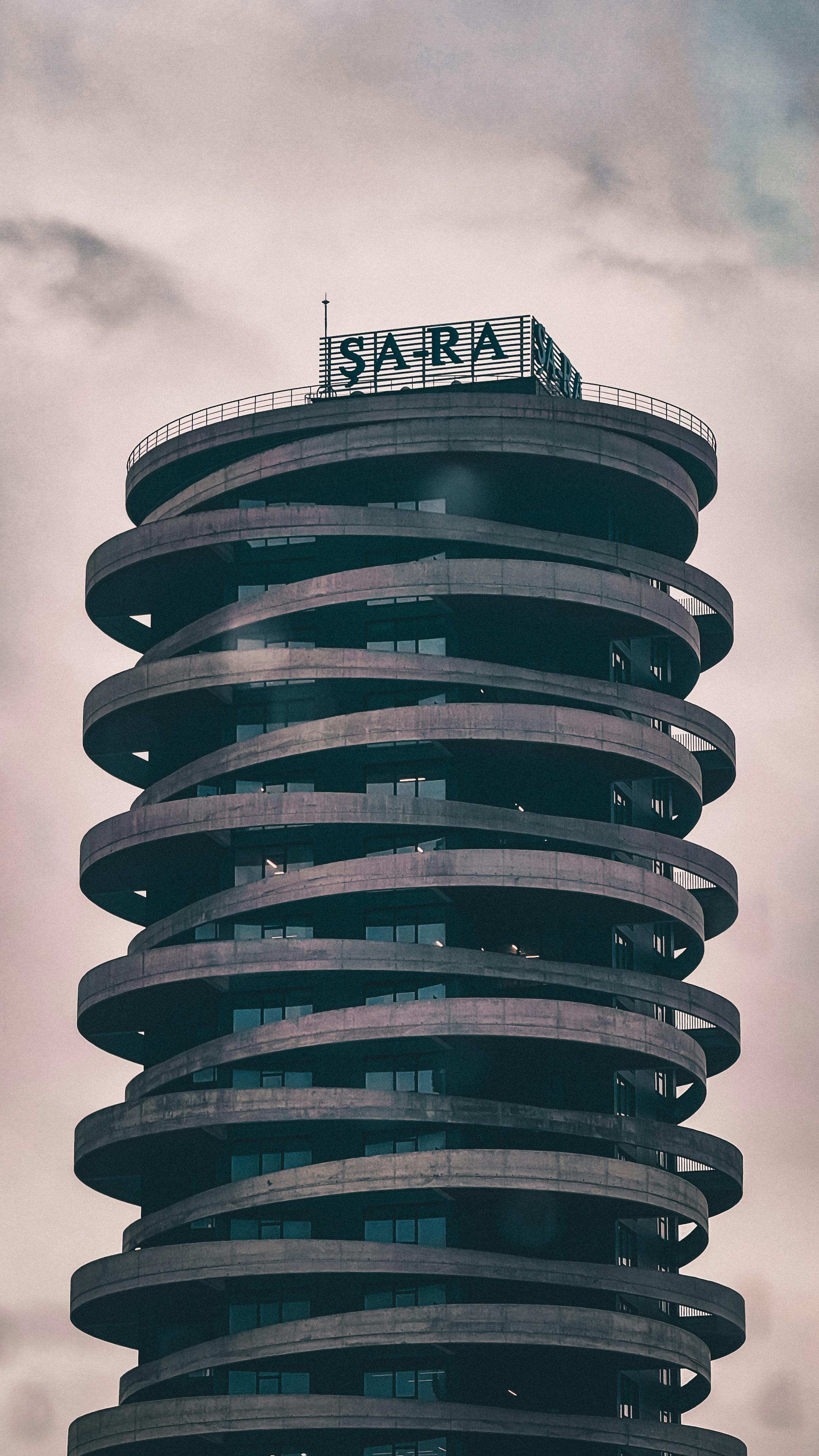 Dramatic view of a modern spiral tower under cloudy skies, featuring unique architectural design.