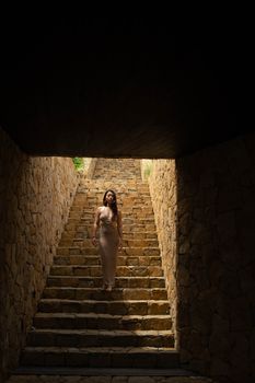 Woman elegantly descending a stone staircase in a dimly lit tunnel.