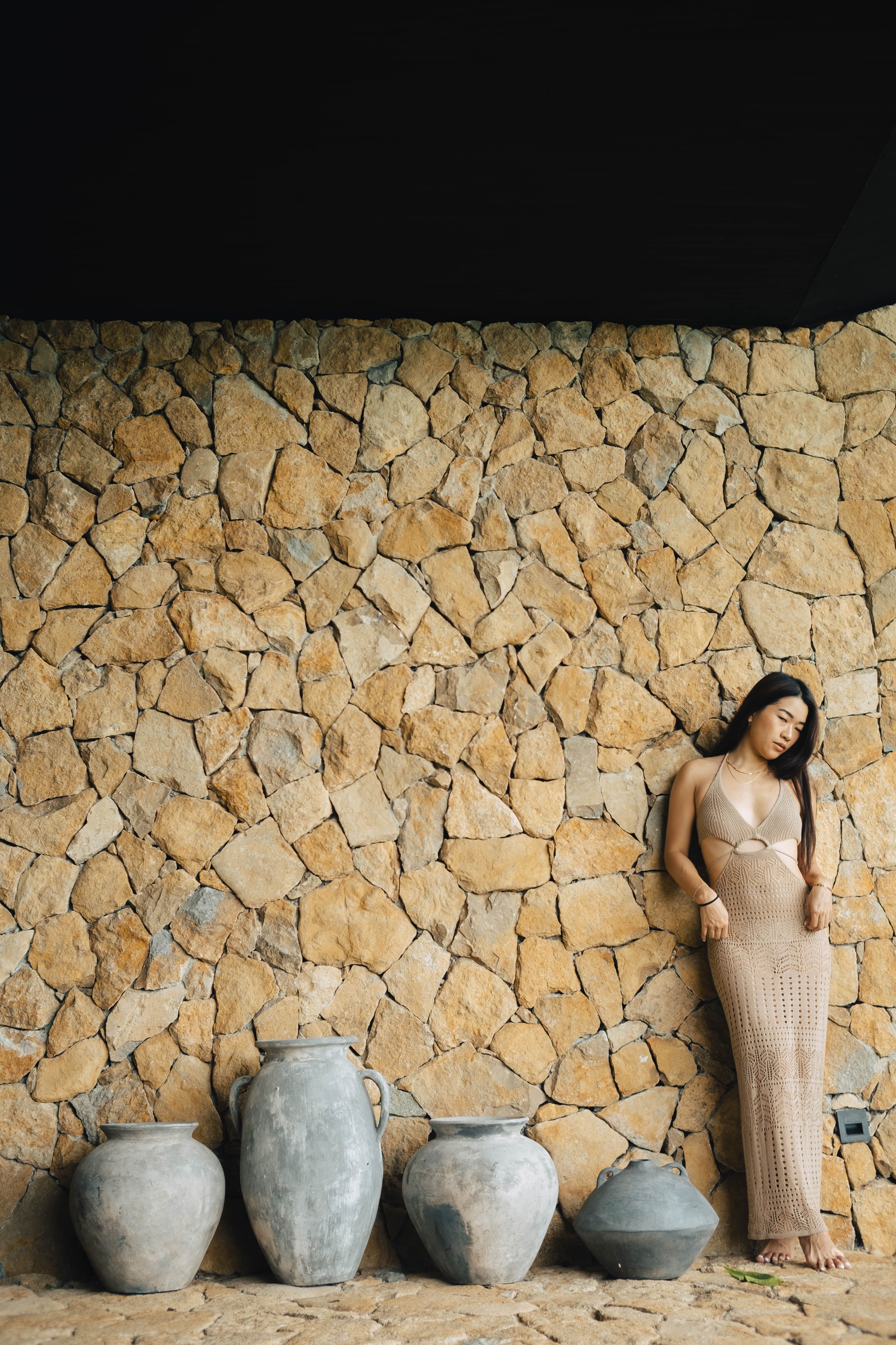 Woman in Beige Dress Leaning on Stone Wall with Vases · Free Stock Photo