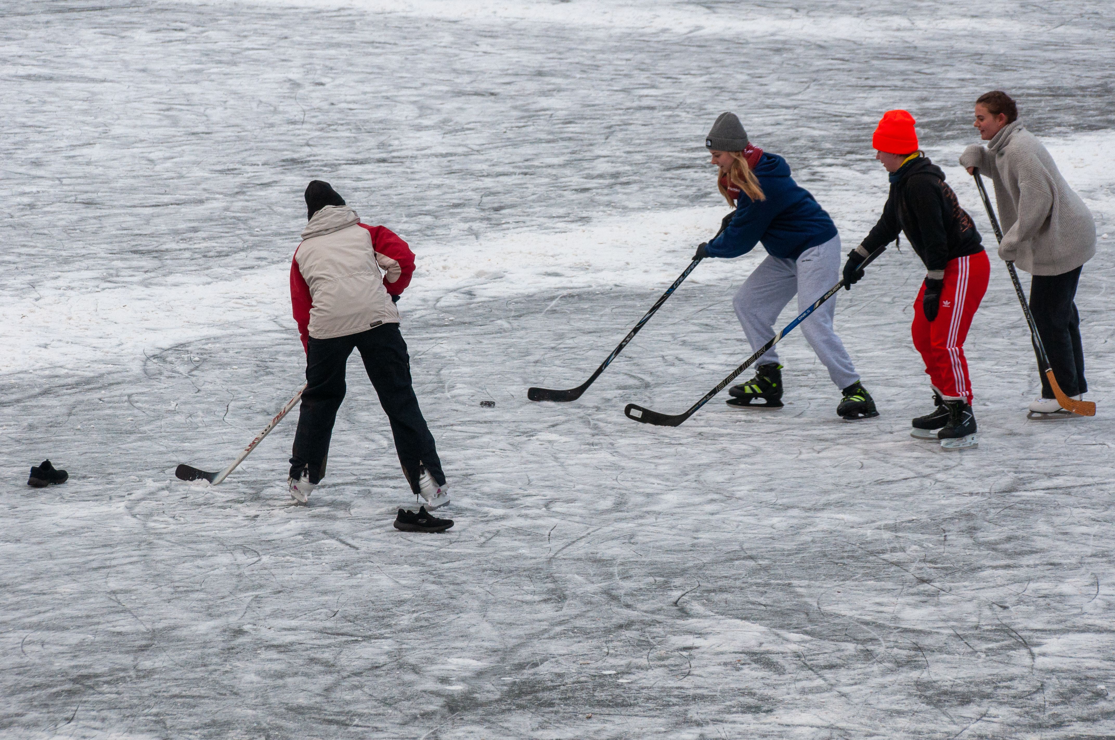 A group of teenagers playing a casual ice hockey game on a frozen lake in winter.