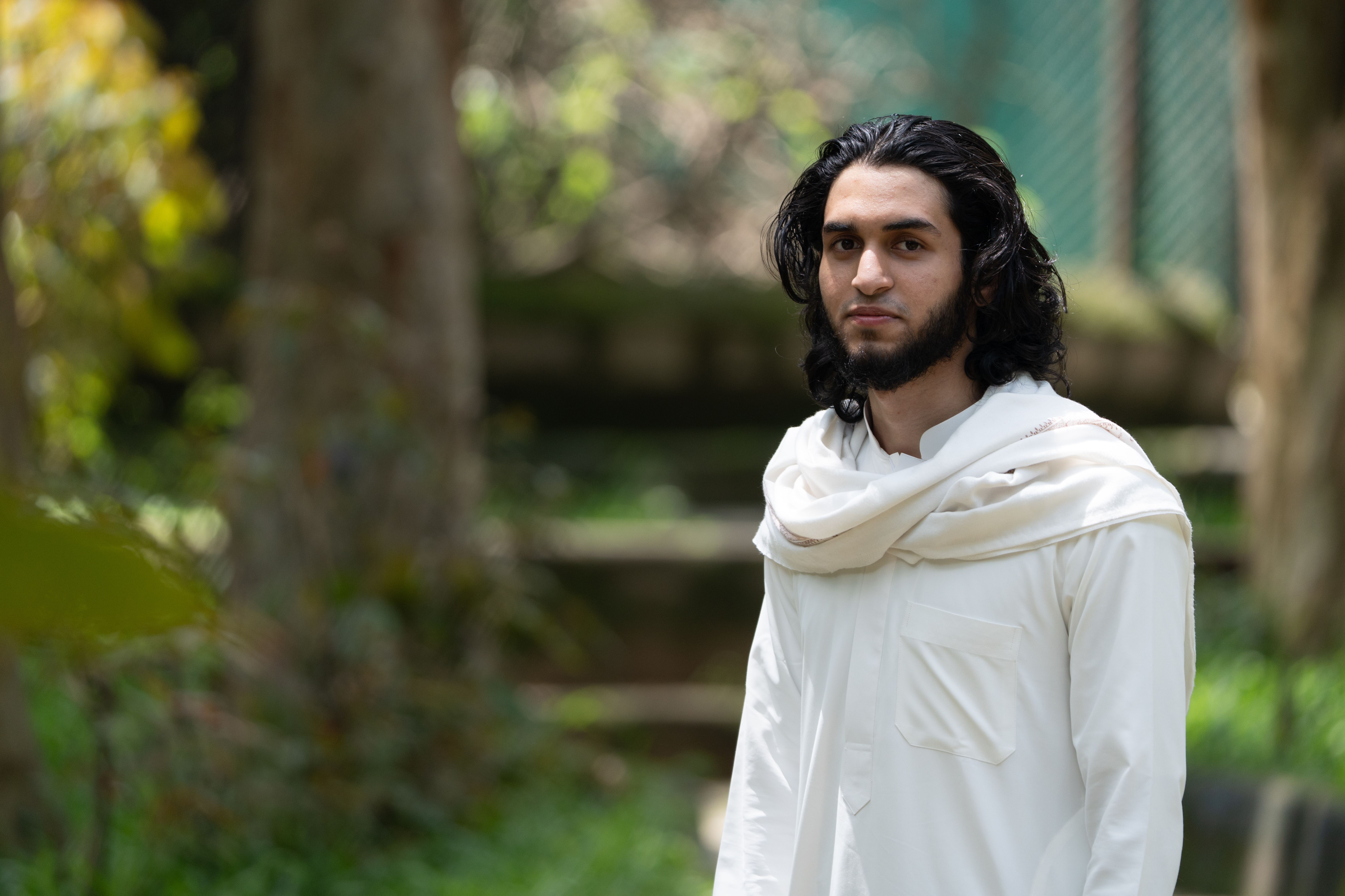 Portrait of a young man with long hair in traditional attire outdoors, serene setting.