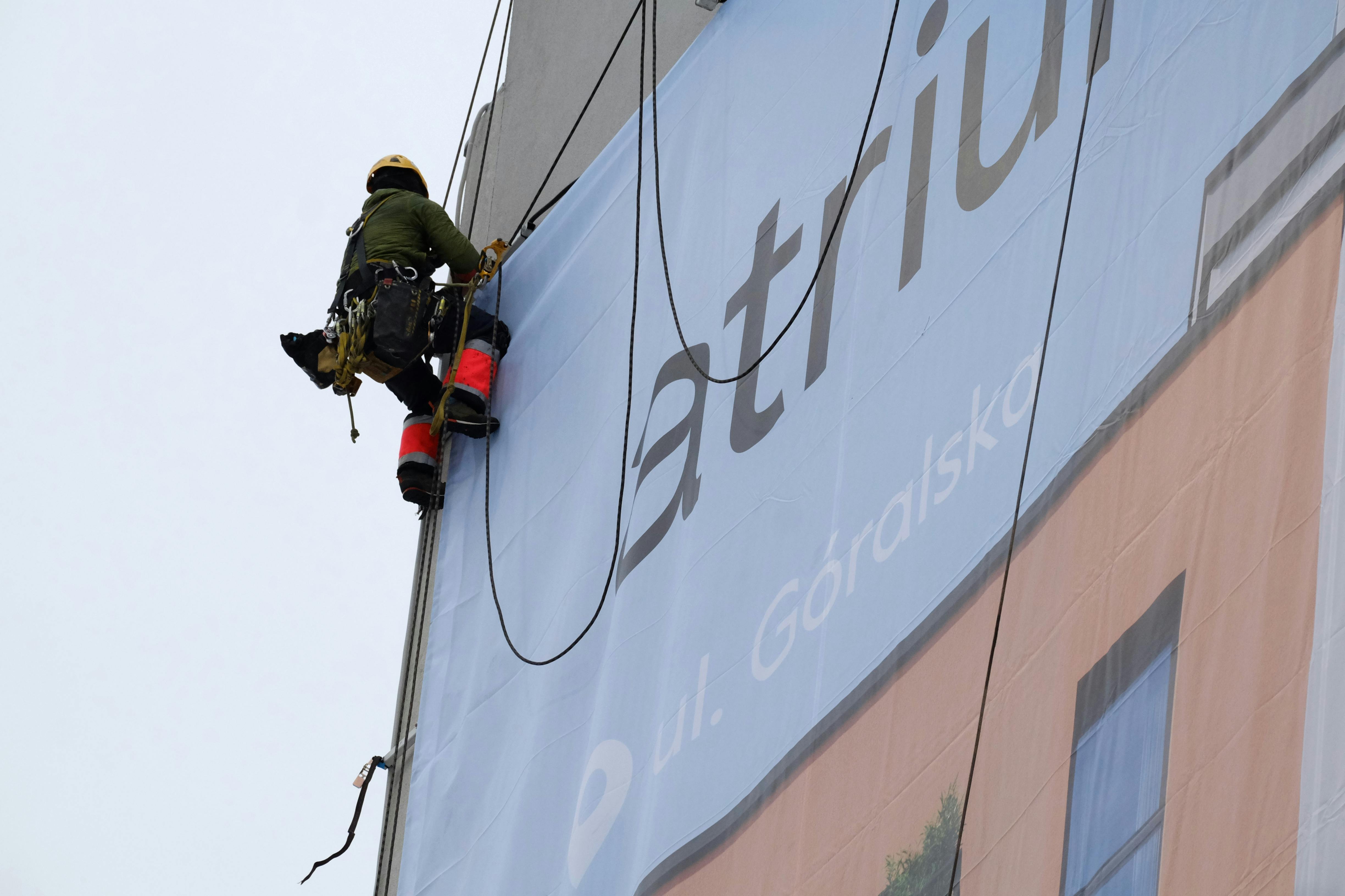 A worker on ropes installs a large banner on a building exterior.