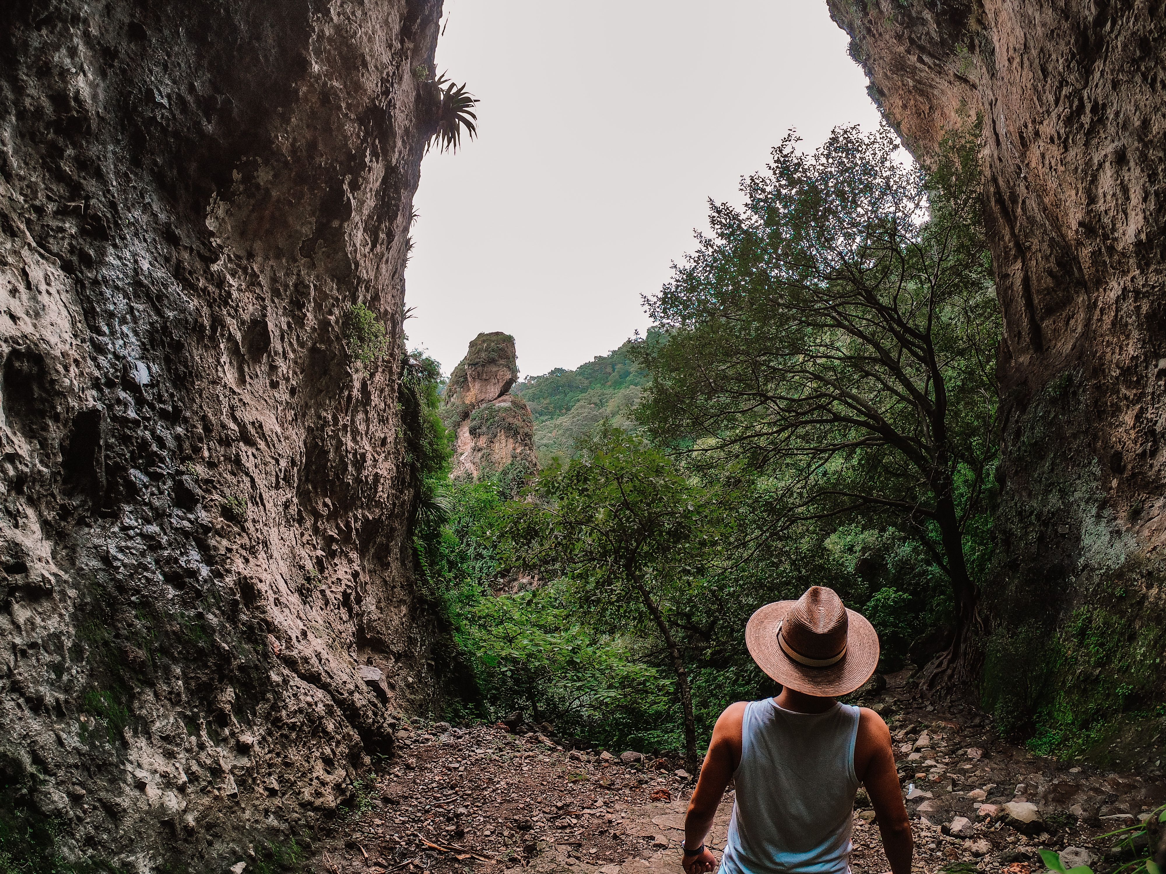 Man with straw hat explores rocky canyon in Tepoztlán, México, surrounded by nature.