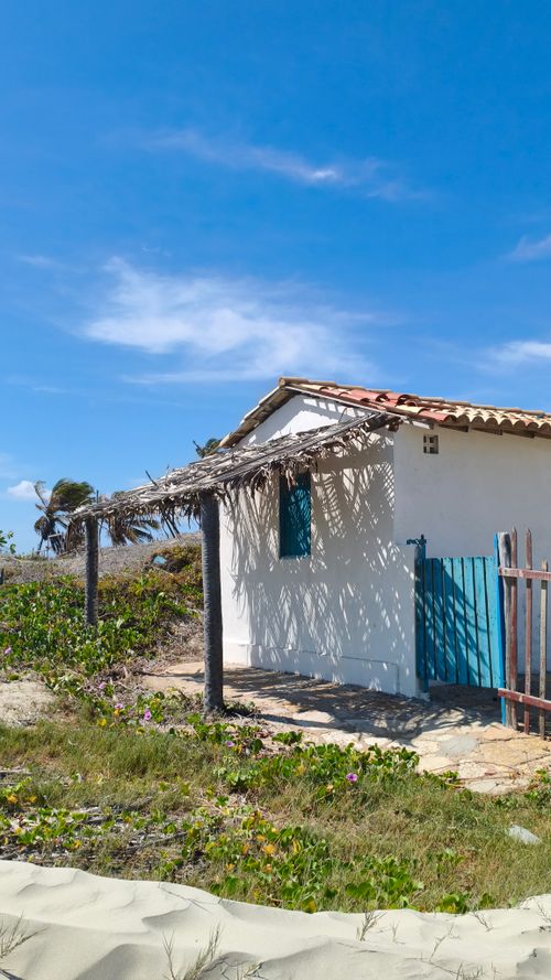 Free A tranquil scene of a rustic beach hut under a clear blue sky, surrounded by greenery. Stock Photo
