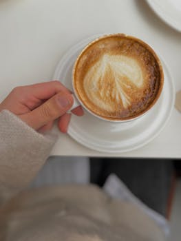 A hand holding a latte with beautiful art in a cozy cafe environment, perfect for relaxation themes.