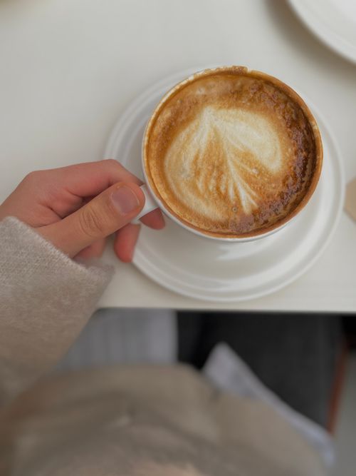 Free A hand holding a latte with beautiful art in a cozy cafe environment, perfect for relaxation themes. Stock Photo
