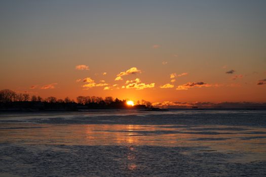 Captivating sunset over a frozen lake with vivid orange sky and silhouetted trees, perfect for travel and nature themes.