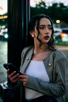 Stylish woman with phone at dusk in lively urban environment.