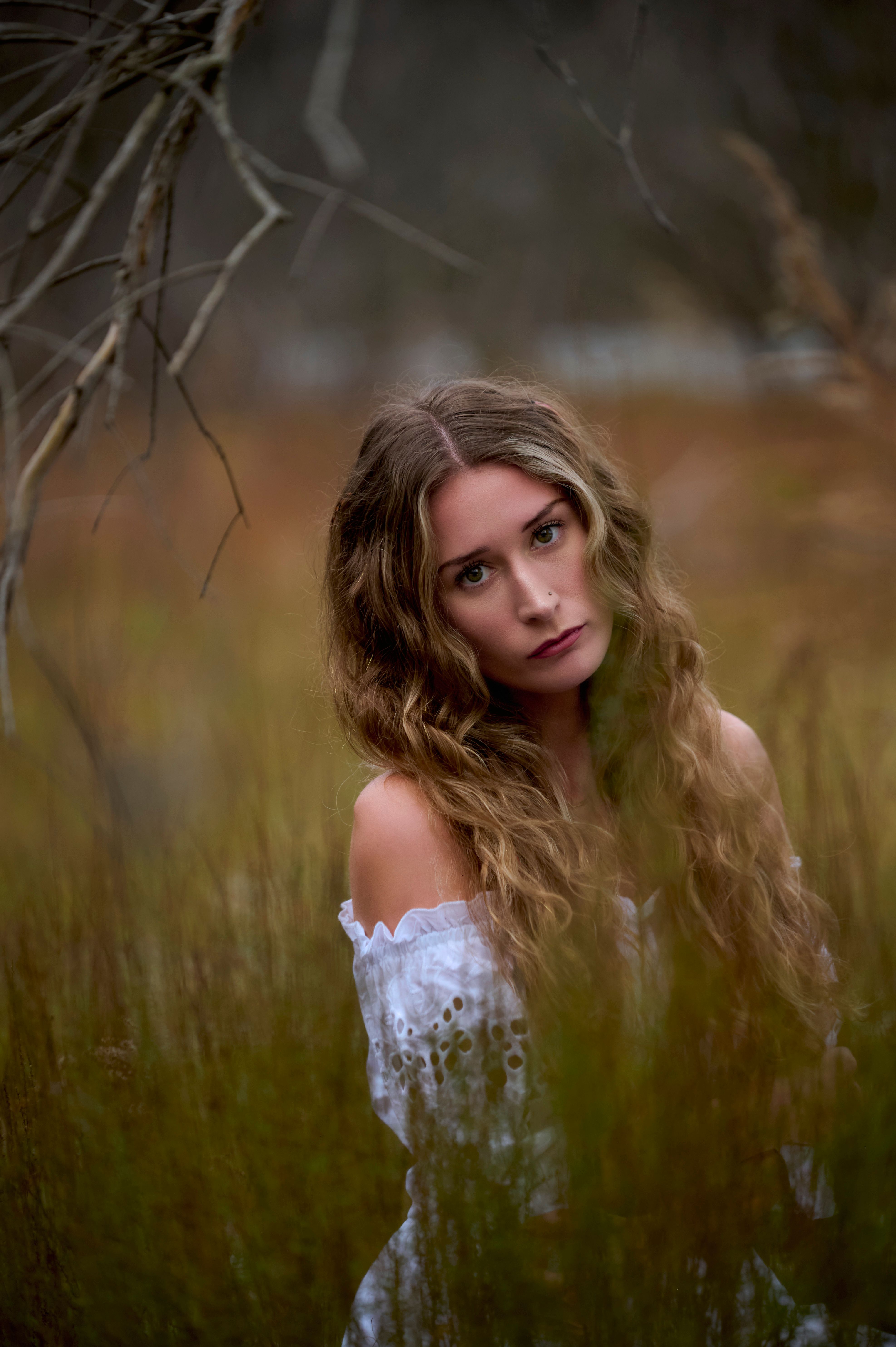 A woman with long hair wearing a white dress in a moody outdoor setting.