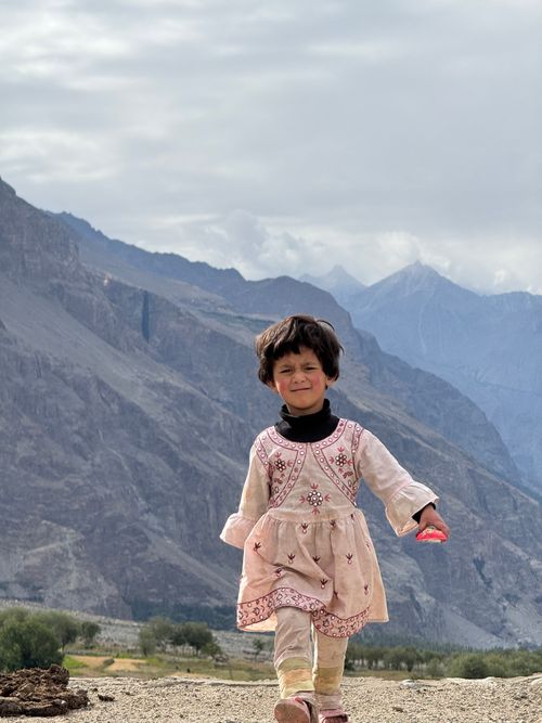 Free A young girl in traditional clothing smiles with majestic mountains in Gilgit-Baltistan. Stock Photo